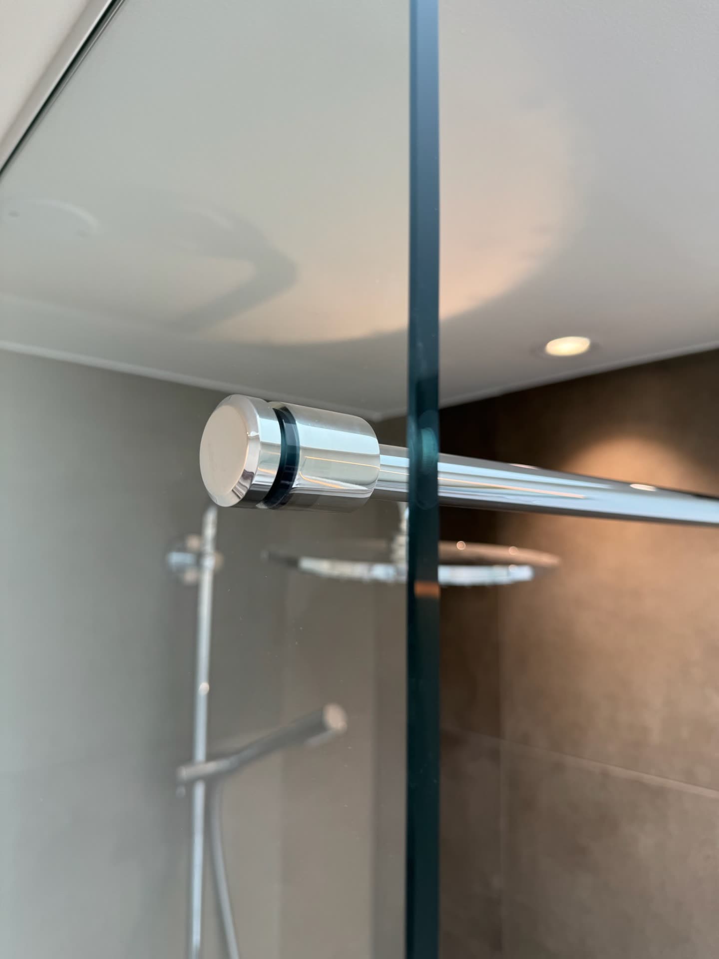 Detalje af blankpoleret beslag på brusevæg i klart glas